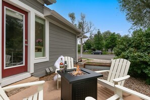 Une terrasse avec une table basse noire dotée d’un foyer, des chaises Adirondack blanches et une porte rouge.