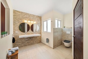Ein modernes Badezimmer mit Steinwand, zwei Waschbecken, einem großen Spiegel und einer Toilette.
