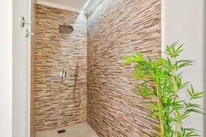 Eine Dusche mit strukturierter Wand, einer Handbrause und einer Bambuspflanze.