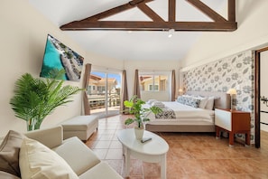 Una habitación amplia con cama, sofá, una mesita y una planta en maceta.