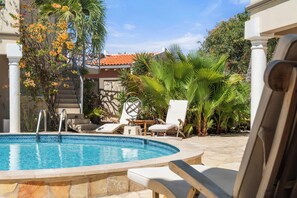 Ein Pool mit Liegestühlen, Palmen und einem Gebäude mit einem Ziegeldach.