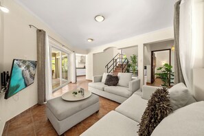 Una sala de estar moderna con un conjunto de sofá, una mesa de centro, un televisor de pantalla plana y una escalera que lleva a otro nivel.