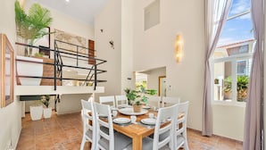 Un coin repas avec une table en bois, des chaises blanches et un escalier agrémenté d’une plante.