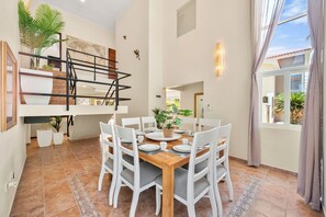Un comedor con una mesa de madera, sillas blancas y una escalera con una planta.
