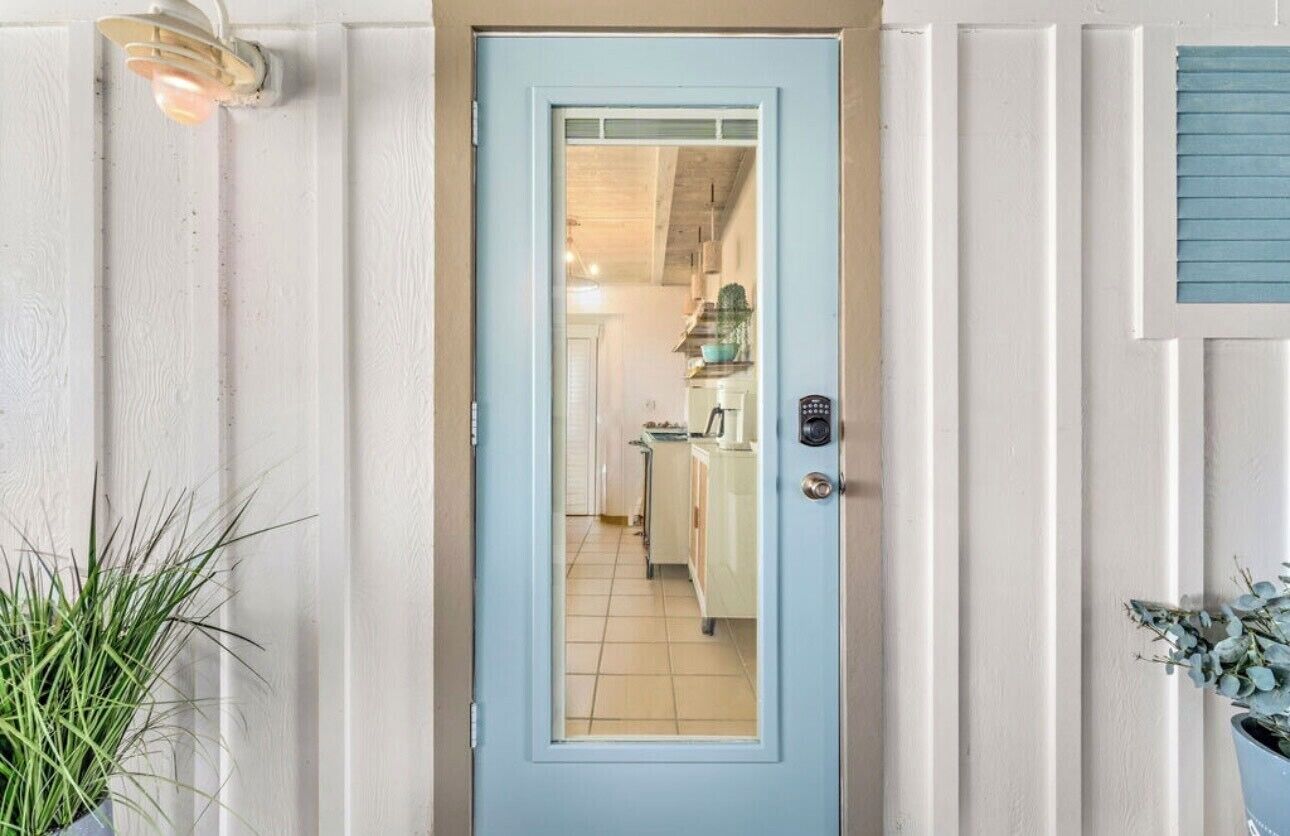 A light blue door leading into a kitchen with white cabinets and a tiled floor.