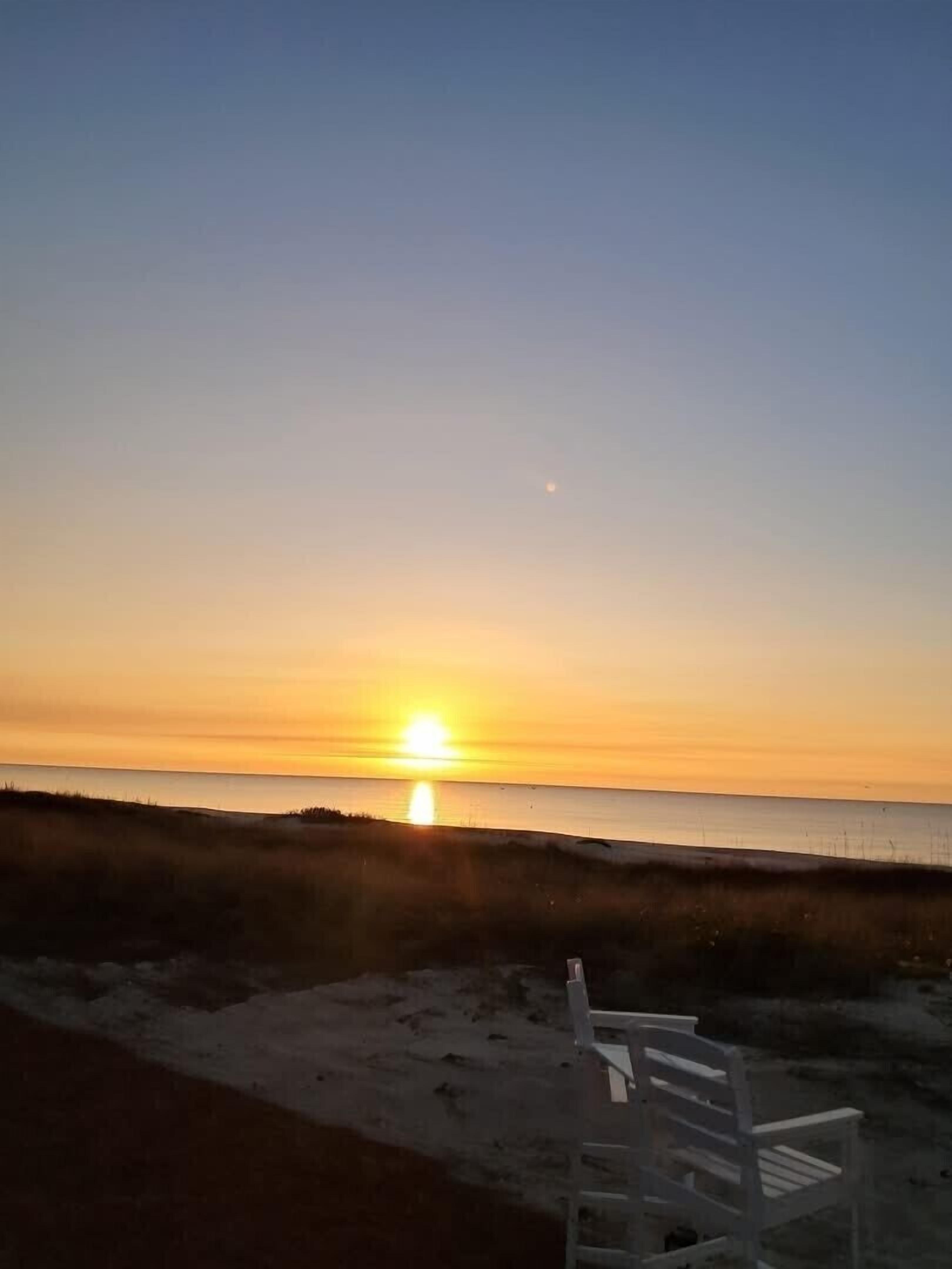 Une scène de plage avec un coucher de soleil, un banc et une mer calme.