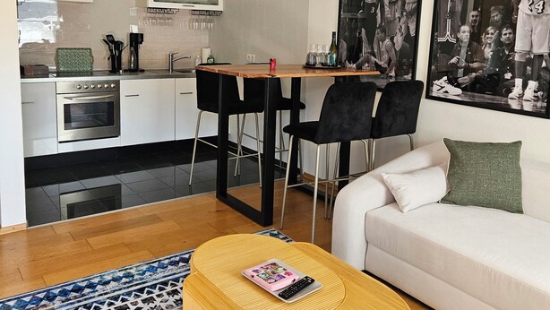 Ein modernes Wohnzimmer mit einer Couch, einem Couchtisch und einem Essbereich mit Stühlen und einem Tisch. An der Wand hängen zwei gerahmte Bilder.
