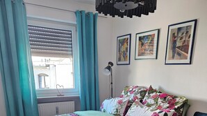 Ein Schlafzimmer mit Bett, Stuhl, Lampe und einem Fenster mit Vorhängen.