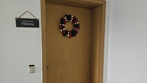 Eine Holztür mit einem Kranz, einem Schild darüber und einer Weihnachtselfigur zur Rechten.