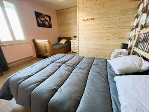 Une chambre à coucher avec un lit, une commode, une table de chevet, une fenêtre et un mur en bois.