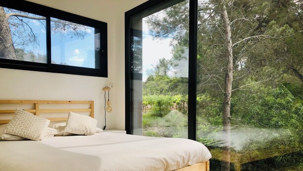 A bedroom with a wooden bed, white bedding, and a large window offering a view of a forested area.