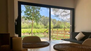 A room with a large sliding glass door leading to a vineyard view. There are two woven placemats on the table, a sofa with a cushion, and a small table with candles.