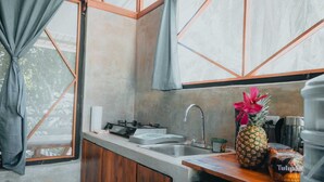 A compact kitchen with a gas stove, sink, and wooden cabinets. A pineapple and a bottle of Tulpam are on the counter. - Kinkajoungalows (Drake Bay)