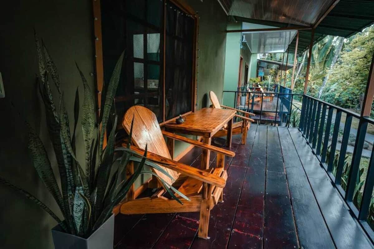 A wooden deck with a table and chairs, surrounded by large plants.