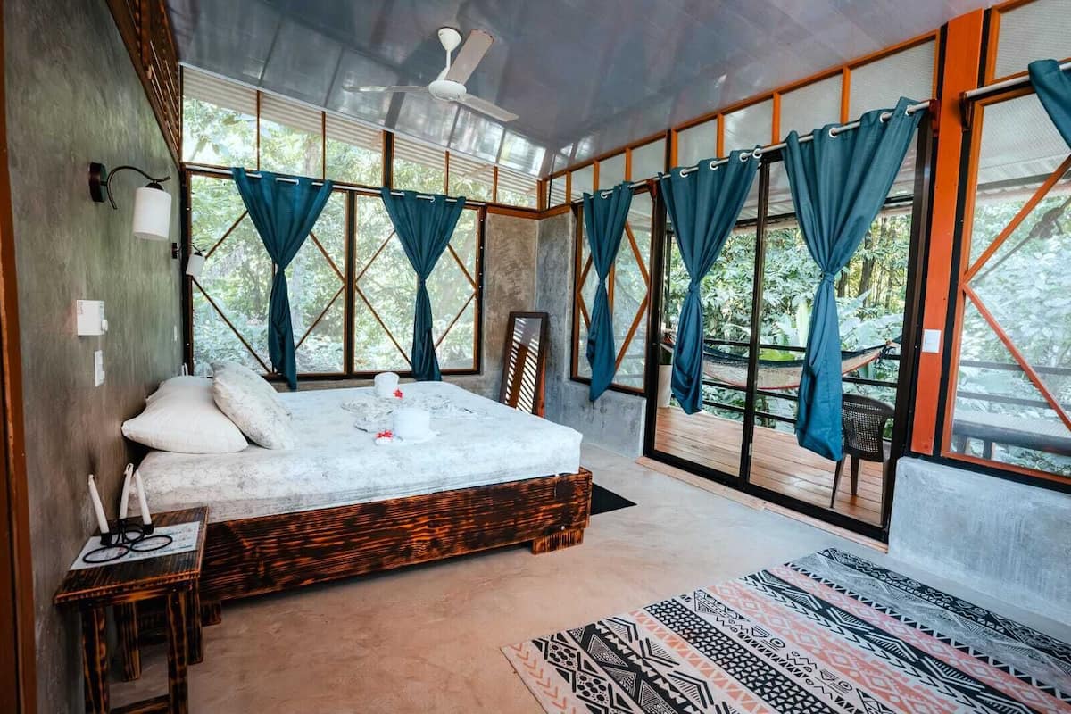 A spacious bedroom with a large bed, a ceiling fan, and multiple windows with curtains.