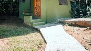 A small, single-story building with a green exterior and a corrugated metal roof. It features a wooden door and a small porch area. - Kinkajoungalows (Drake Bay)