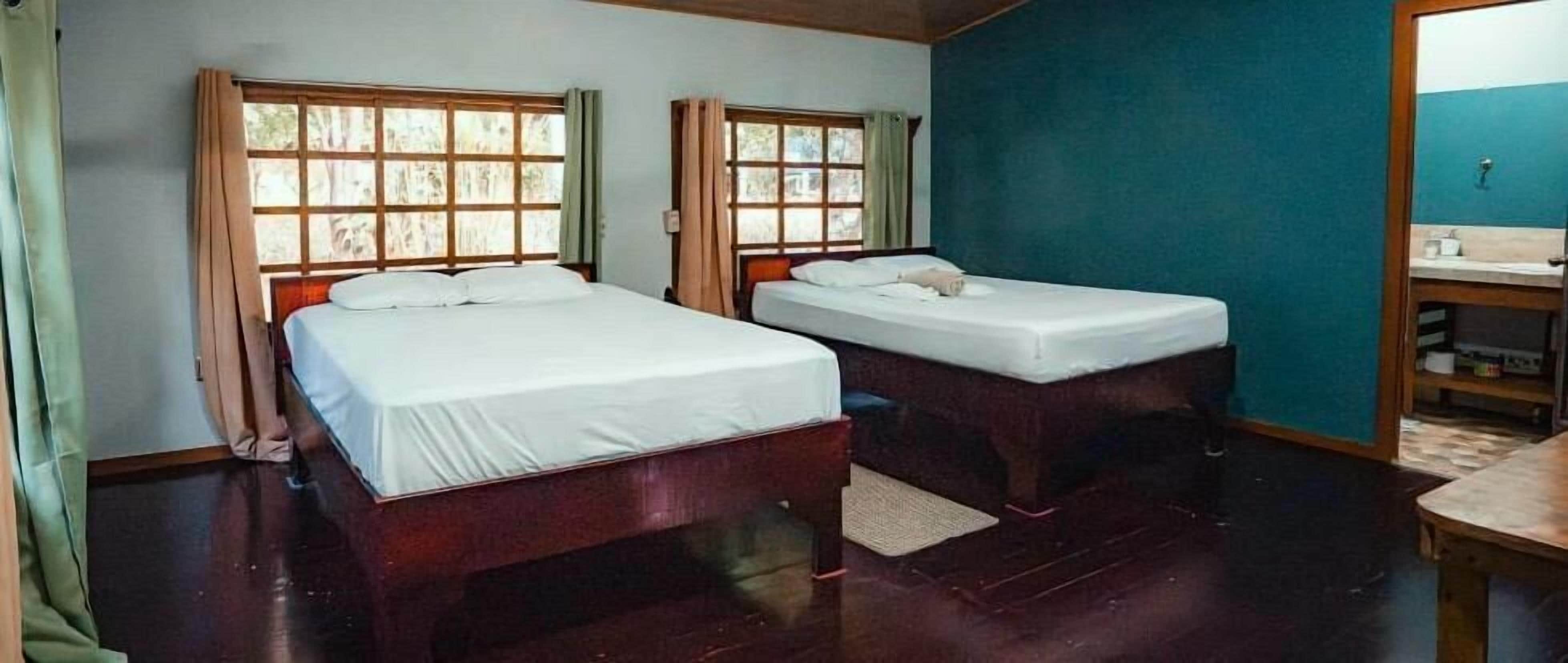 Een kamer met twee bedden, een houten vloer en een badkamer met een wastafel en spiegel.
