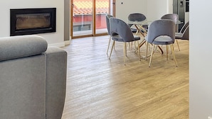 Een moderne woonkamer met een open haard, een grijze bank, een eettafel met stoelen en een grote schuifdeur die uitkomt op een balkon.