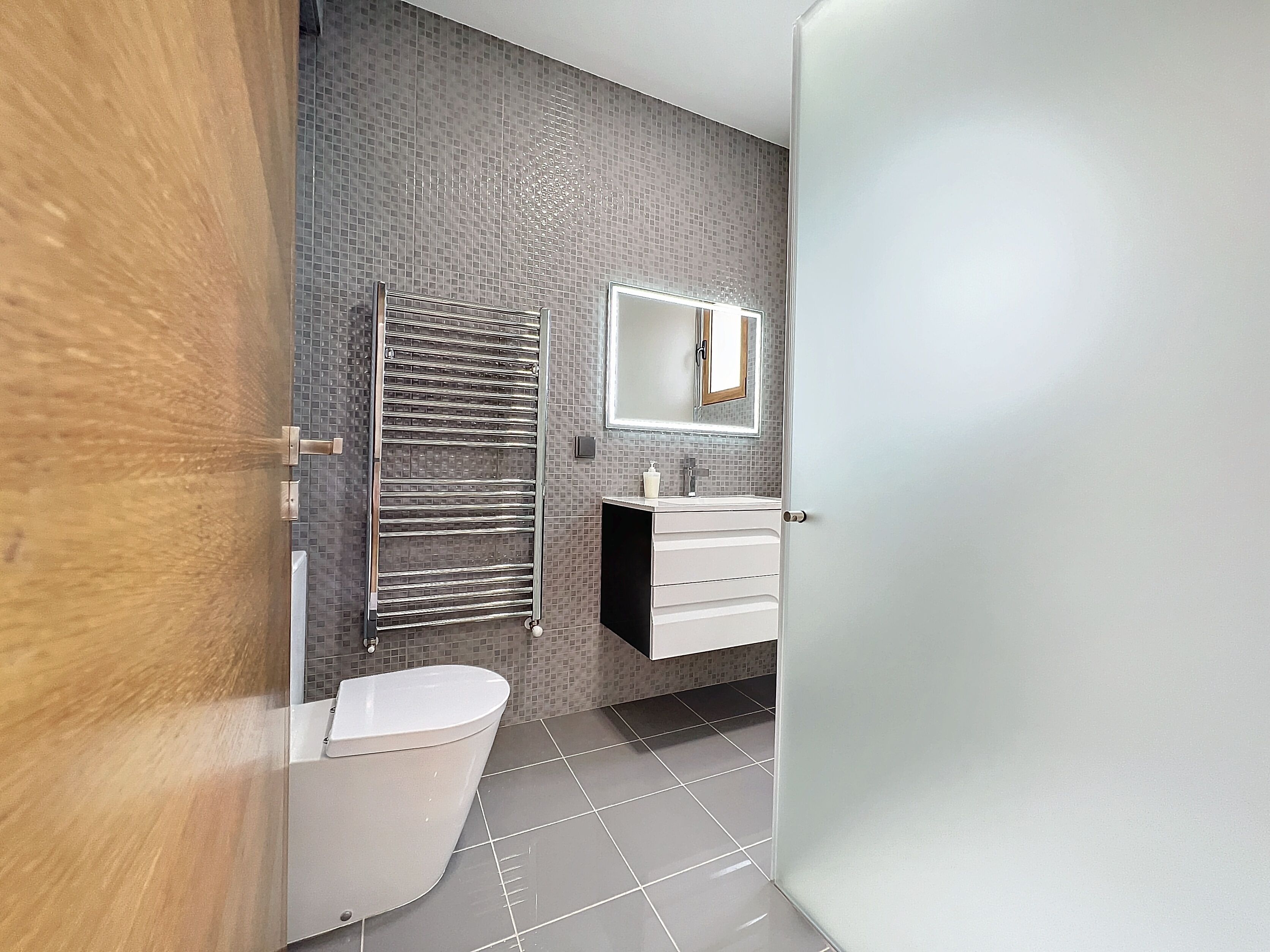 A modern bathroom with a toilet, a towel rack, a mirror, and a sink.
