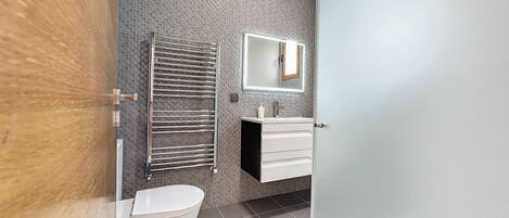 A modern bathroom with a toilet, a towel rack, a mirror, and a sink.