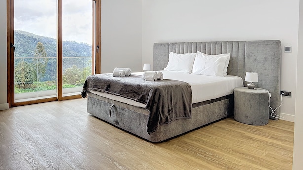 Een moderne slaapkamer met een groot bed, een nachtkastje en uitzicht op een bergachtig landschap door een glazen schuifdeur.