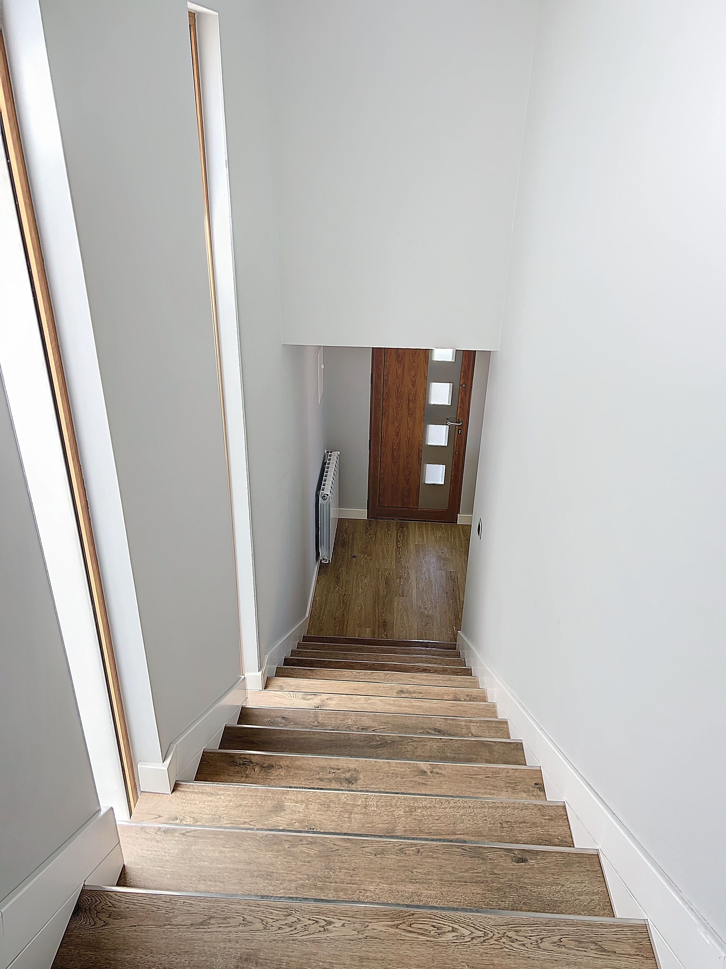 Un escalier avec des marches en bois menant à un palier où se trouvent un radiateur et une porte.