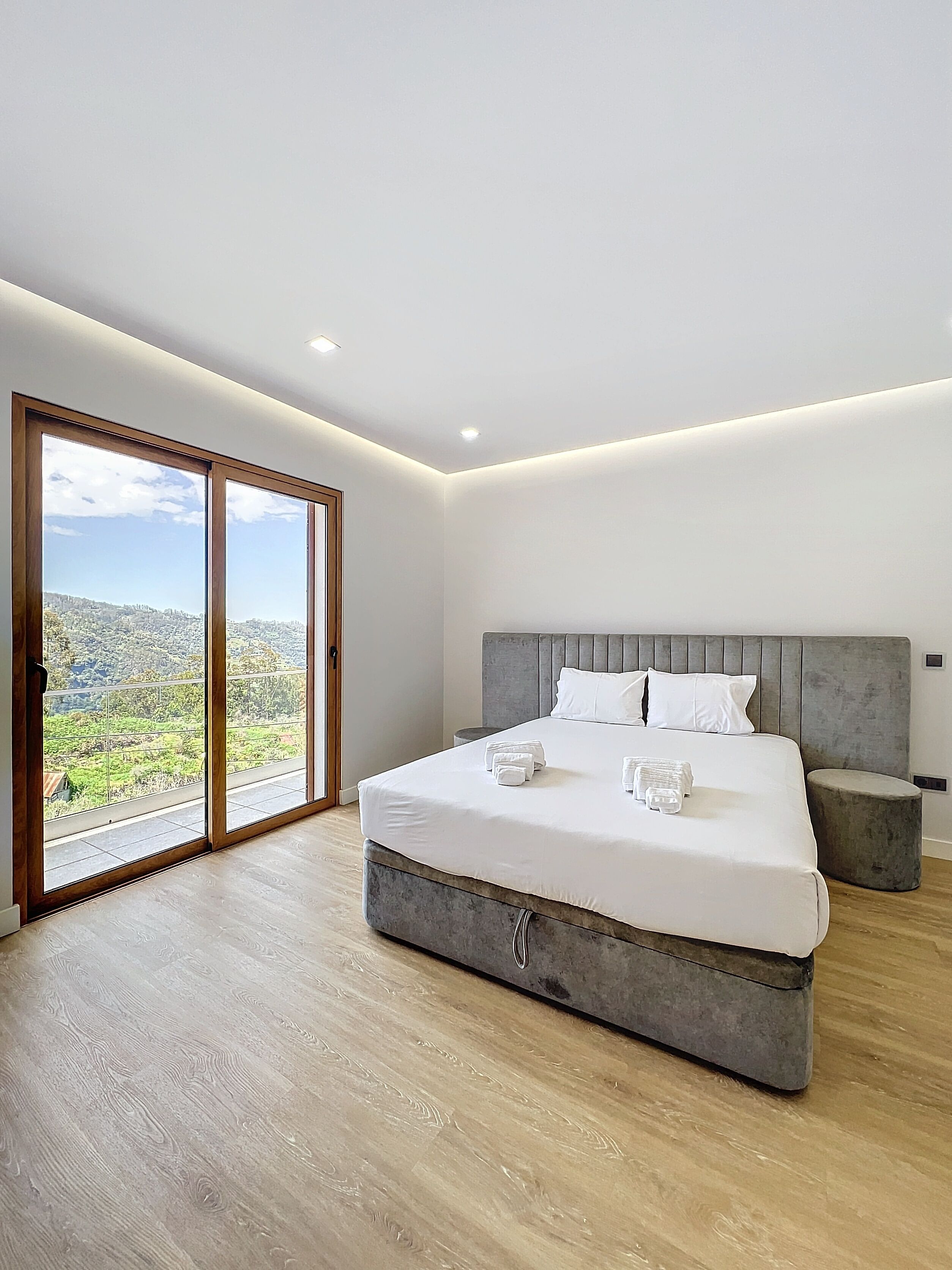 Une chambre avec un grand lit, une vue à travers les portes coulissantes et une tête de lit grise.