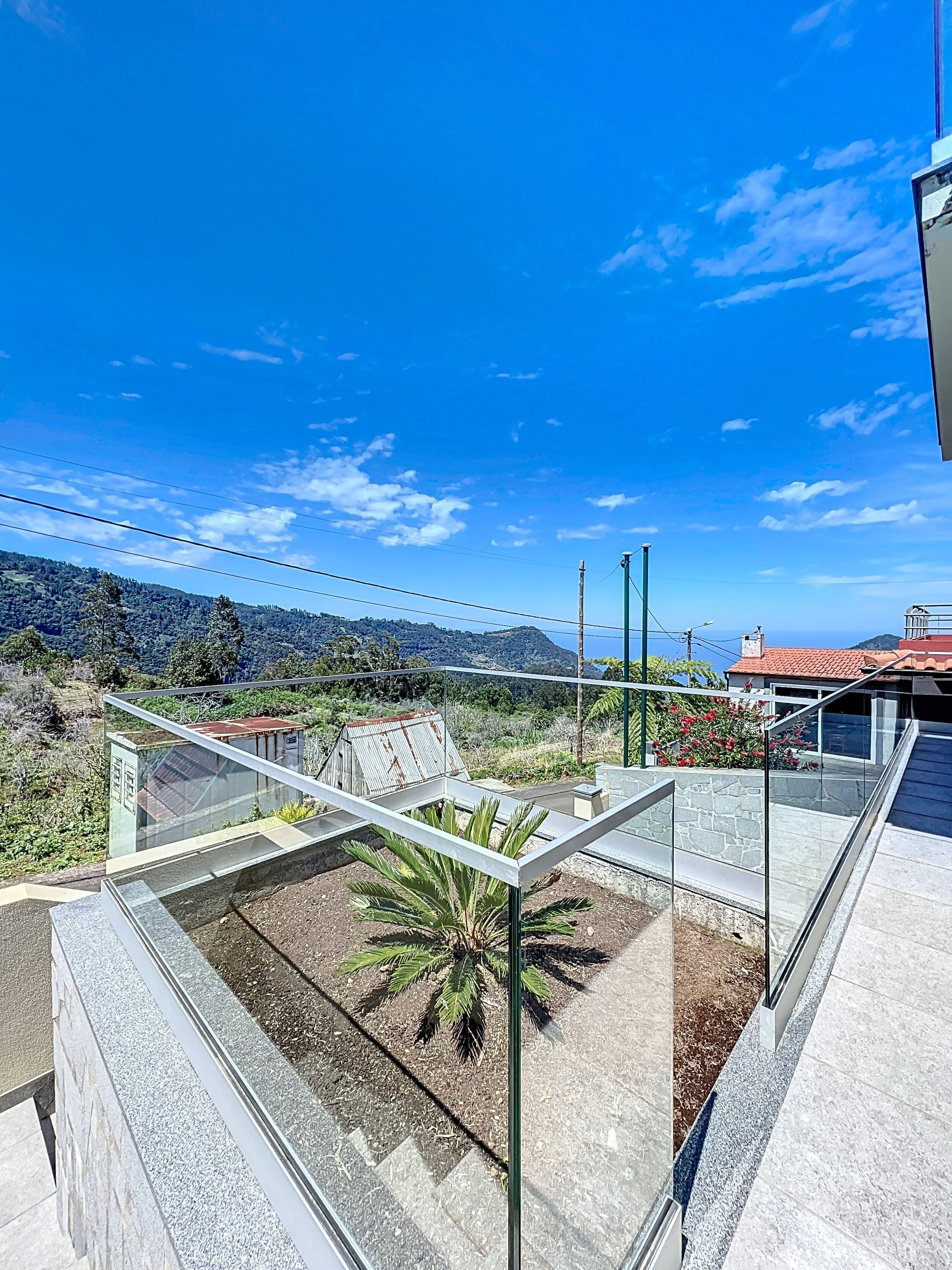 A modern glass-enclosed balcony with a view of a mountainous landscape and a clear blue sky.