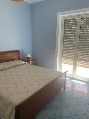 A bedroom with a bed, a nightstand, a lamp, and a sliding door to a balcony.