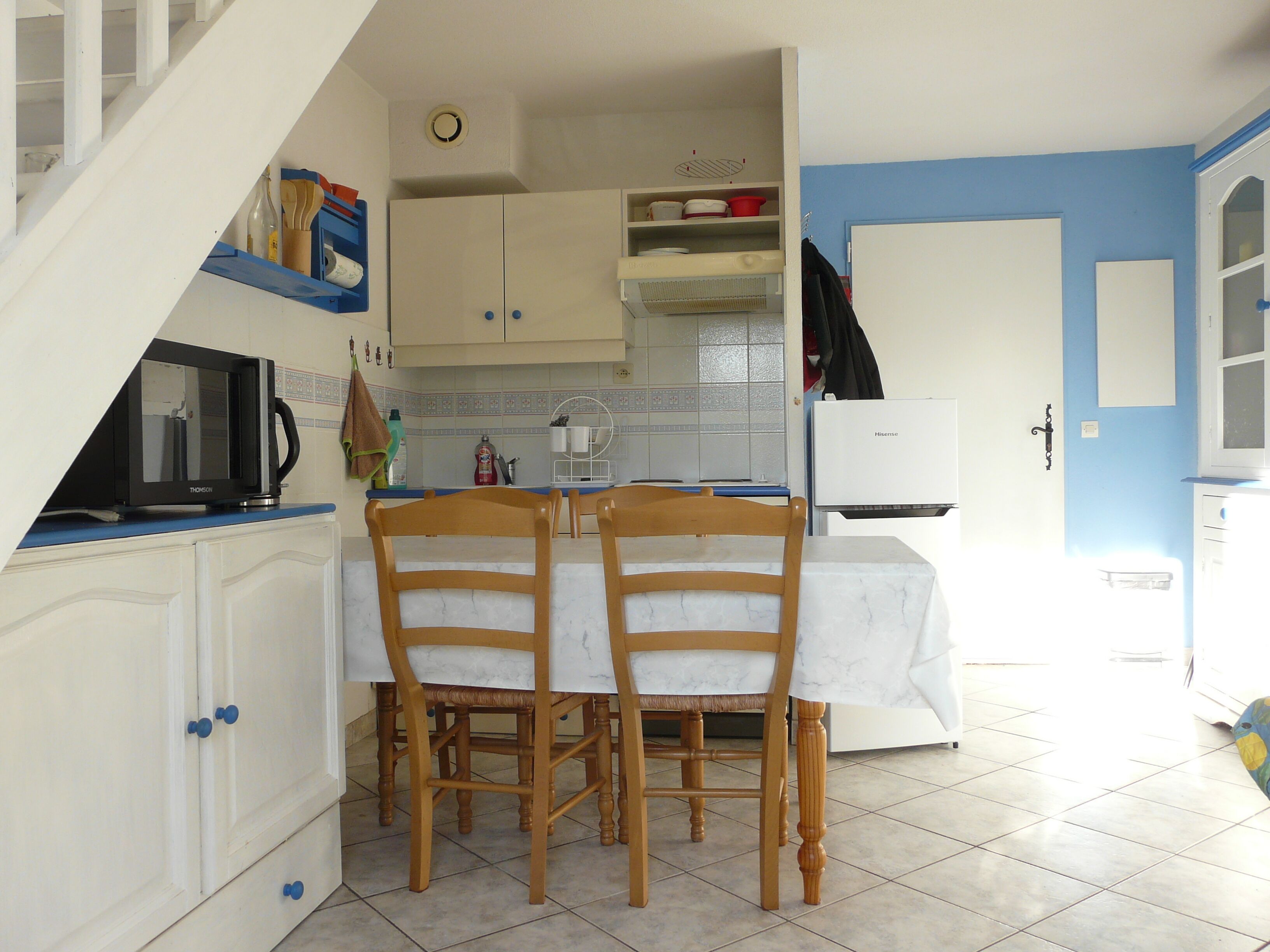 A kitchen with two wooden chairs, a table, white cabinets, a microwave, and a refrigerator.