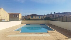 Una piscina rectangular con suelo de baldosas, rodeada por un muro bajo y una cerca.
