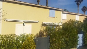 Un edificio con fachada amarilla, contraventanas blancas y entrada protegida por una verja.