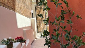 A narrow corridor with tiled flooring, potted plants, and a metal gate in the background. - Joli Studio à 2 Minutes du Centre de Monaco (Beausoleil)