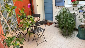 An outdoor patio with a table and chairs, surrounded by potted plants and a window with a view. - Joli Studio à 2 Minutes du Centre de Monaco (Beausoleil)