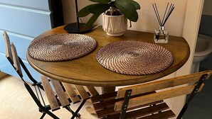 A round wooden table with woven placemats, two chairs with metal frames, a potted orchid, a floor lamp, and a small glass container with reed sticks. - Joli Studio à 2 Minutes du Centre de Monaco (Beausoleil)