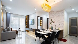 A modern living room with a sofa, dining table, and chairs. There is a chandelier, a TV, and a window with curtains. - Midtown My Hung Quan 7-Luxury Apartment (Ho Chi Minh City)