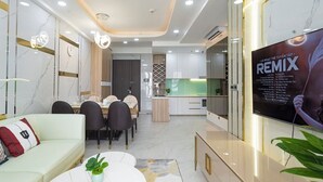 A modern living room with a sofa, dining table, and chairs, a kitchen area with a TV, and a poster on the wall. - Midtown My Hung Quan 7-Luxury Apartment (Ho Chi Minh City)