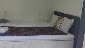 A small, single-bed room with a wooden floor, a simple bed with a dark headboard, and a single light fixture on the ceiling. - Minivilla in Gustavsvik, Nacka (Värmdö)