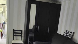 A living room with a dark grey sofa, a glass coffee table, a wooden chair, and a black wardrobe. - Minivilla in Gustavsvik, Nacka (Värmdö)