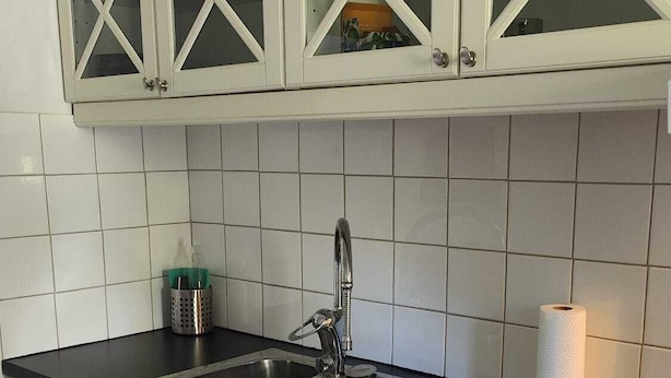 A kitchen with white cabinets, a black countertop, a stainless steel sink, and a paper towel roll. - Minivilla in Gustavsvik, Nacka (Värmdö)
