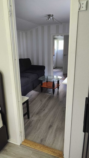 A living room with a dark-colored sofa, a glass-top coffee table, and a wooden floor. - Minivilla in Gustavsvik, Nacka (Värmdö)