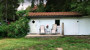 A small white building with a tiled roof, a porch with two chairs, and a small garden area. - Minivilla in Gustavsvik, Nacka (Värmdö)