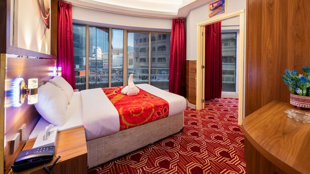 Una camera d'albergo con un letto grande, una scrivania con il telefono e vista sulla città attraverso ampie finestre.