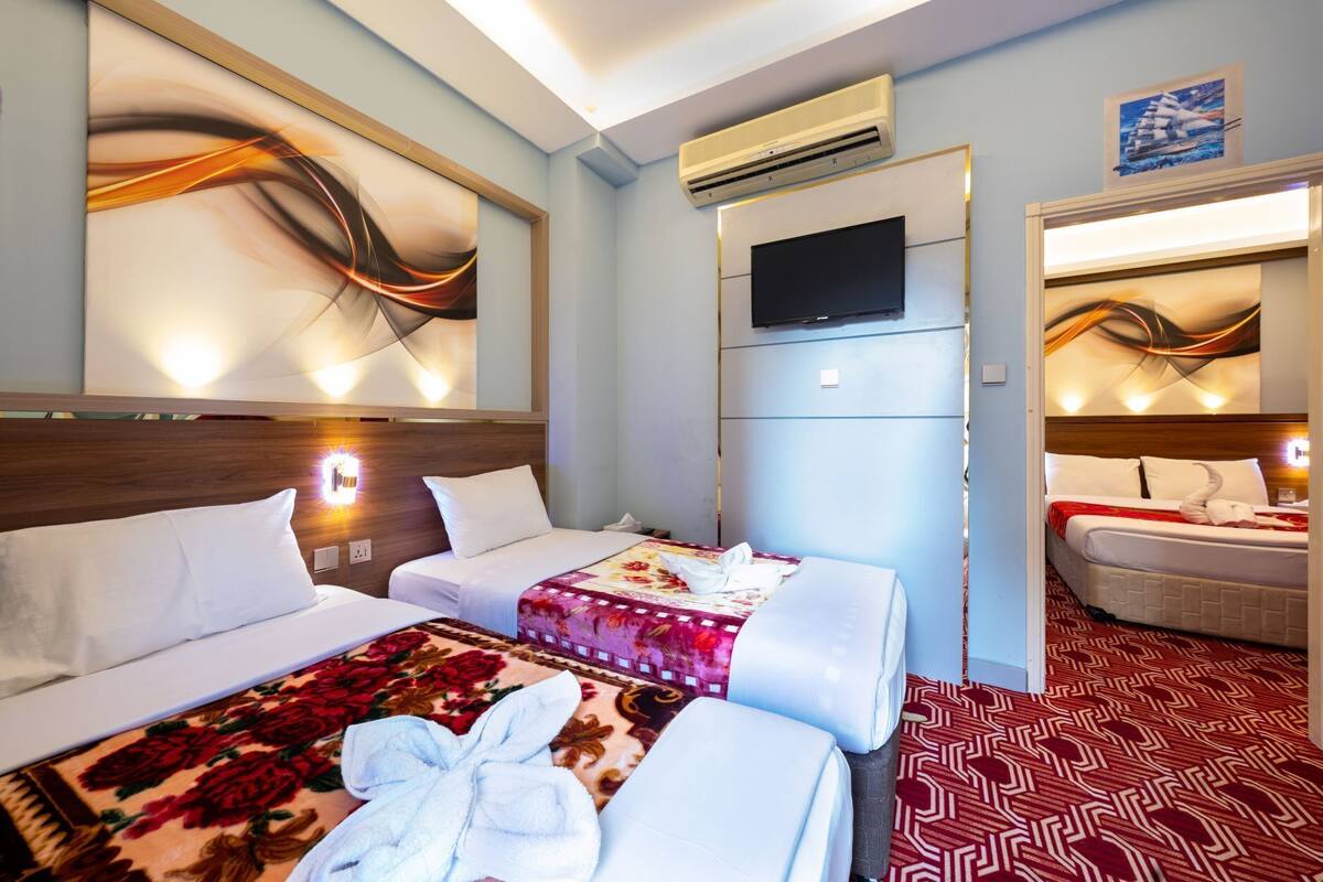 A hotel room with two beds, a flat-screen TV, an air conditioner, and a decorative mirror.