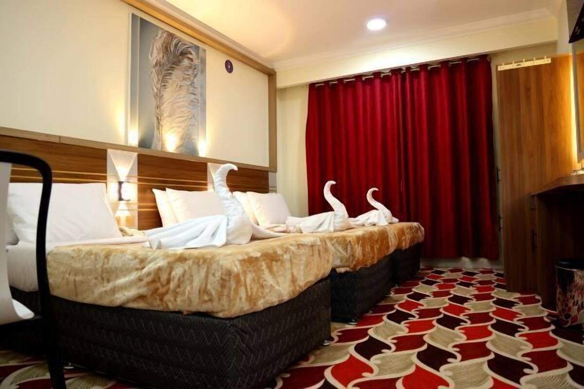 A hotel room with two beds, a red curtain, a patterned carpet, and a wall-mounted artwork.