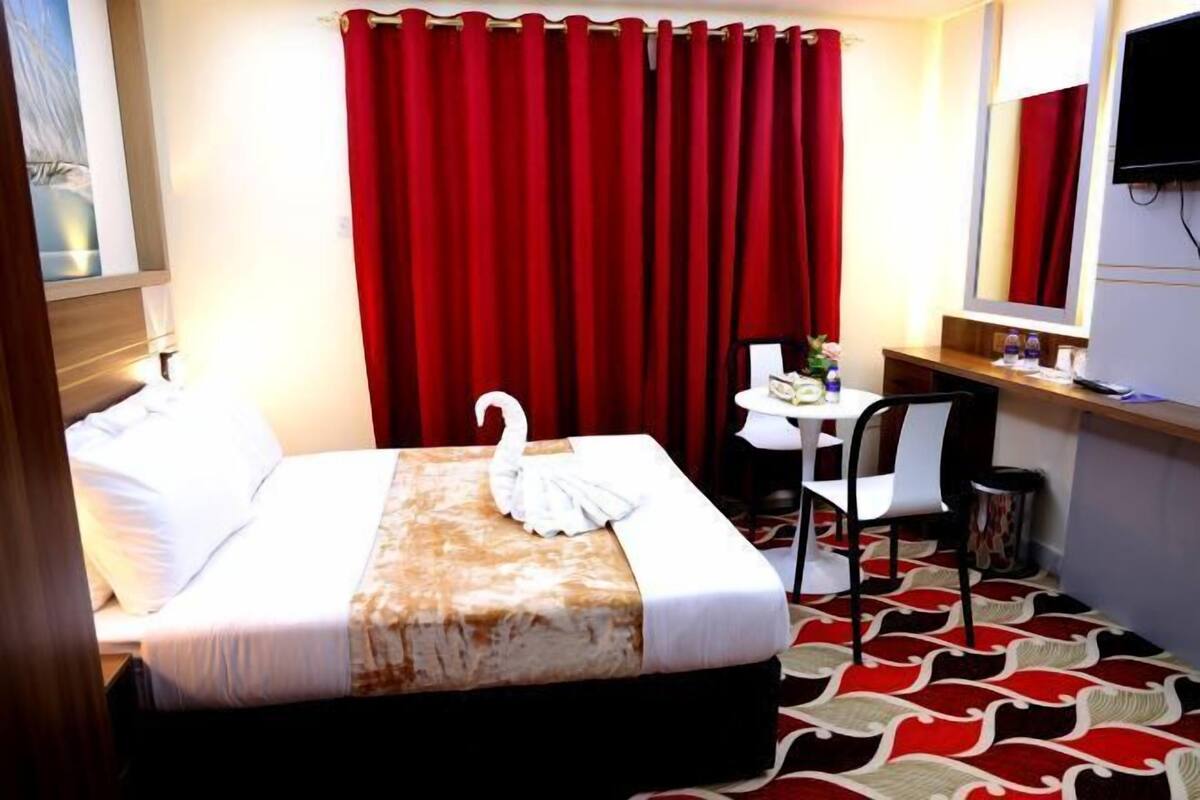A hotel room with a bed, a desk, a chair, a television, and a red curtain.