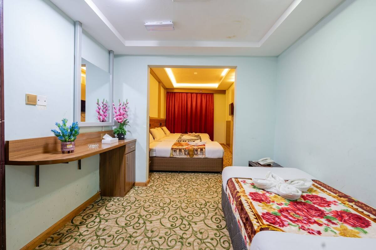 A hotel room with a bed, a bedside table with a mirror, a desk with a chair, and a bathroom visible through an open door.