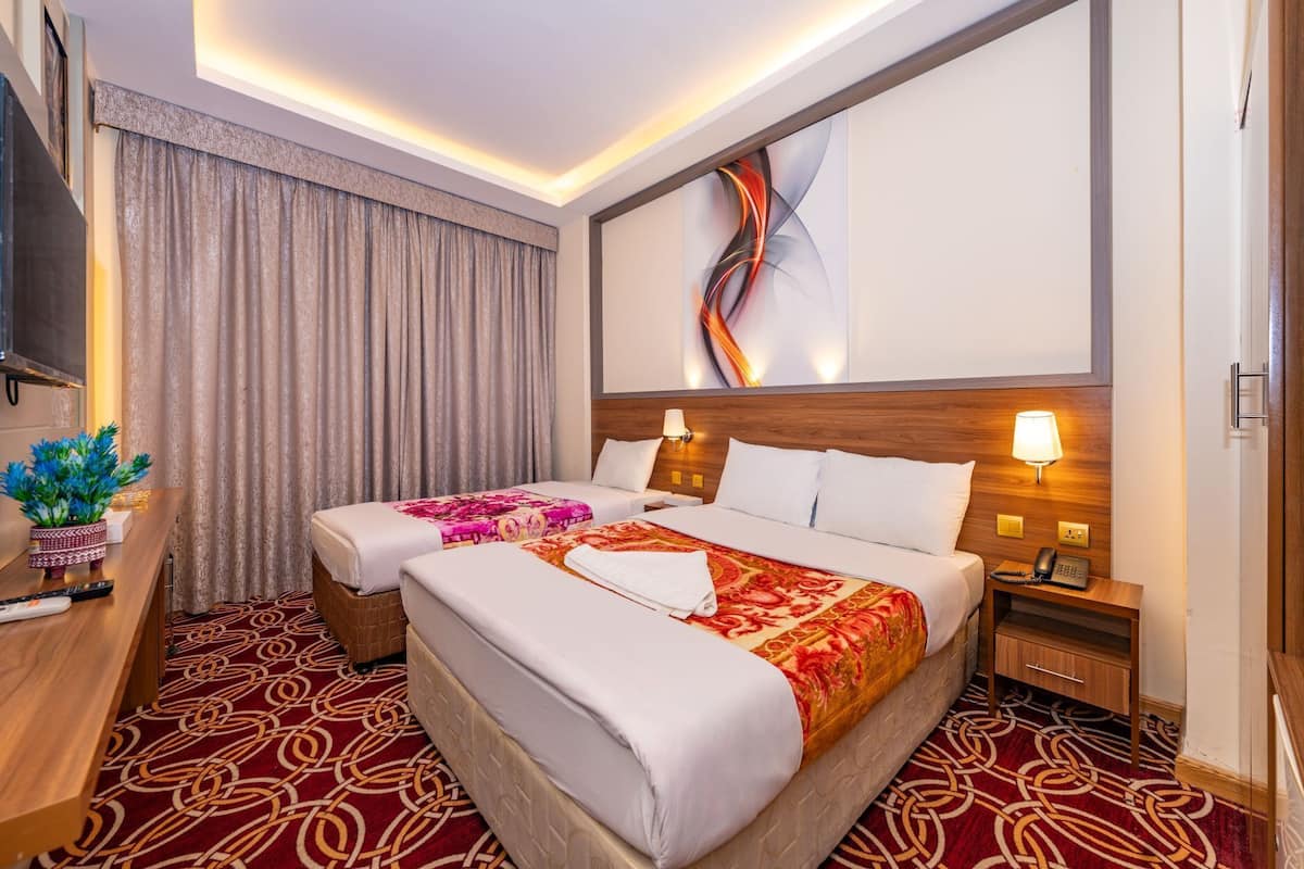 A hotel room with two beds, a desk, a lamp, and a wall art piece.