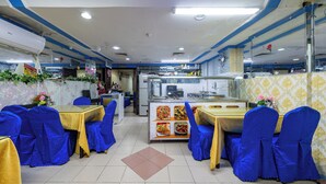 Un ristorante con sedie e tavoli rivestiti di blu, un'area cucina e un pavimento piastrellato.