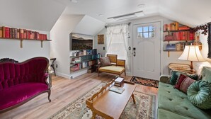 A cozy loft apartment with a red velvet sofa, a green tufted sofa, a wooden coffee table, and a bookshelf filled with books. - The Victorian Story at Midtown Manor (Bend)